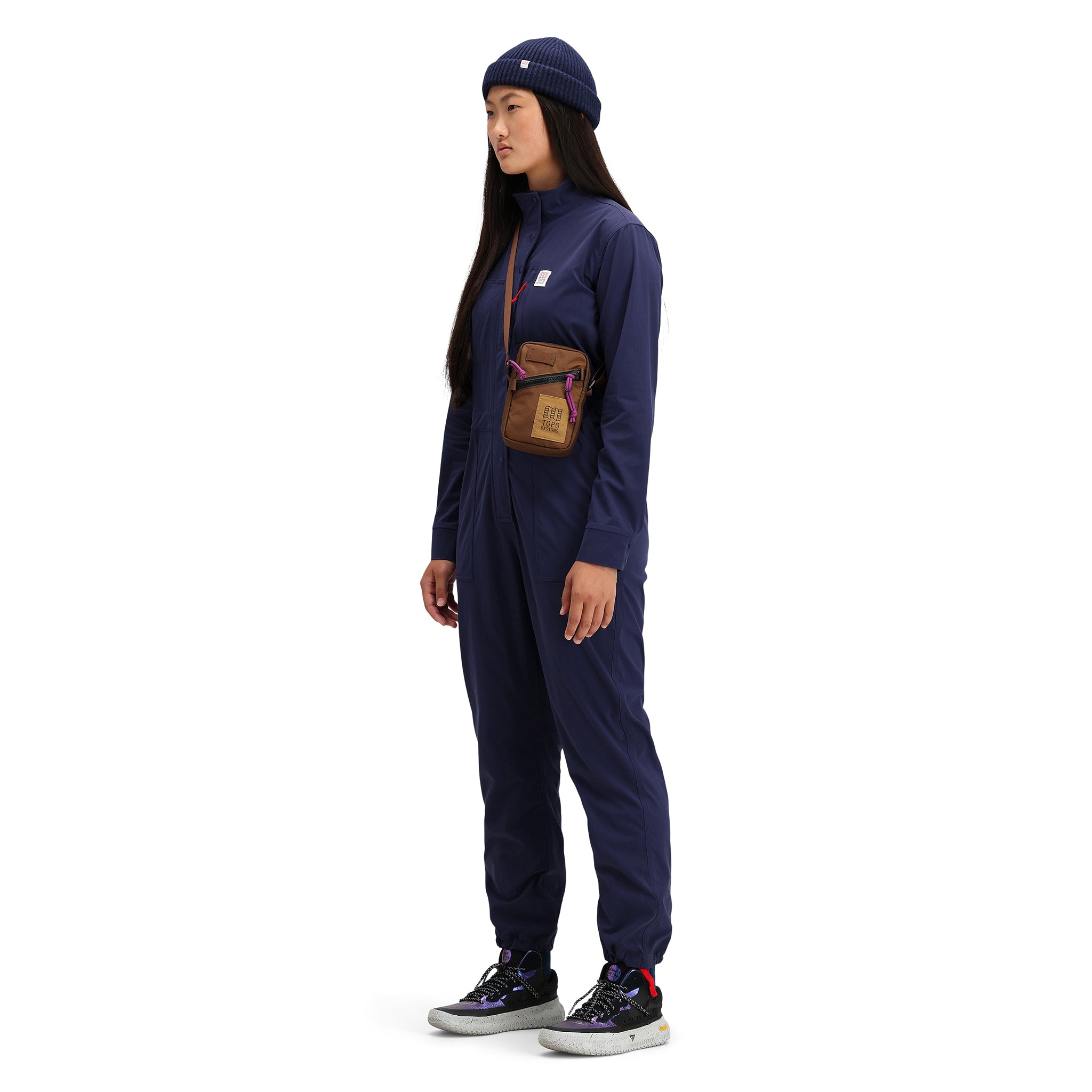 General side shot of model wearing Topo Designs Women's Coverall jumpsuit in "Navy" blue. 