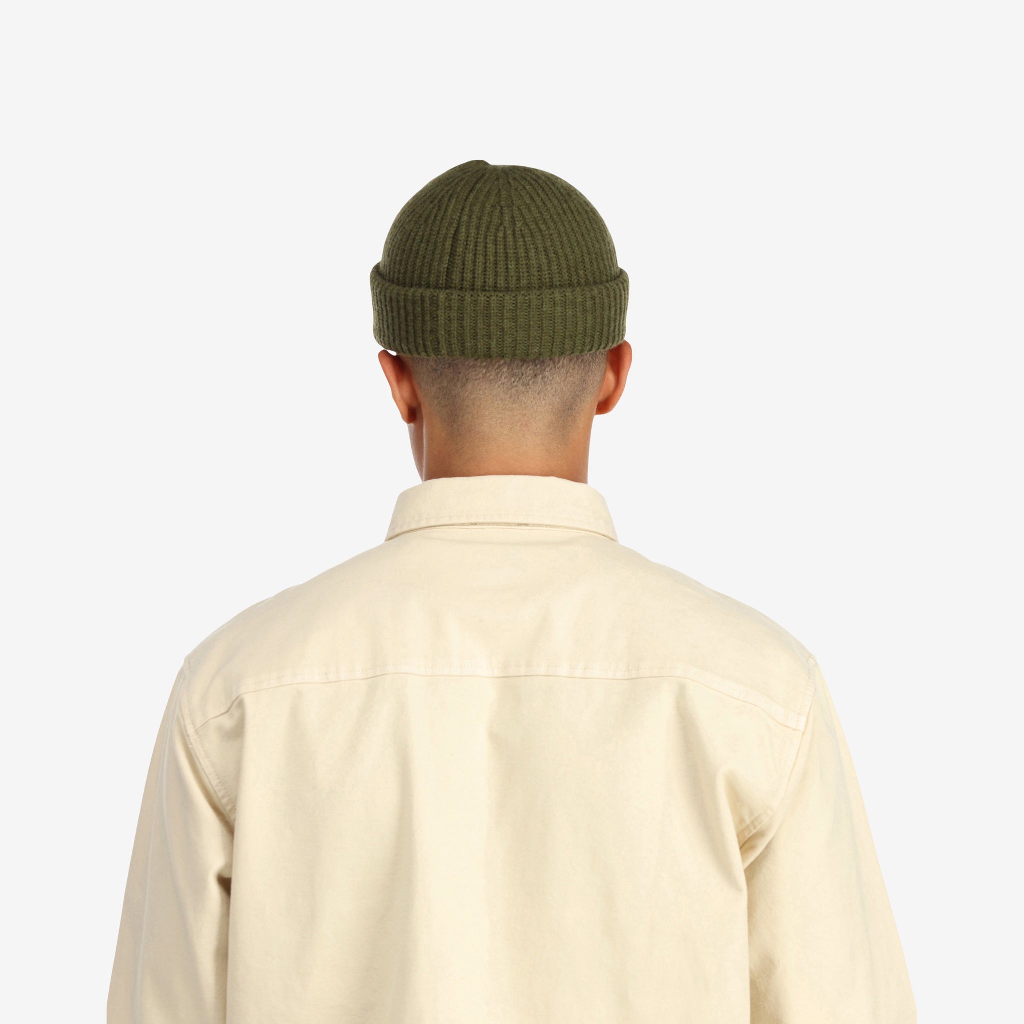 Back model shot of Topo Designs Global Beanie merino wool blend watchman cap in "olive" green.