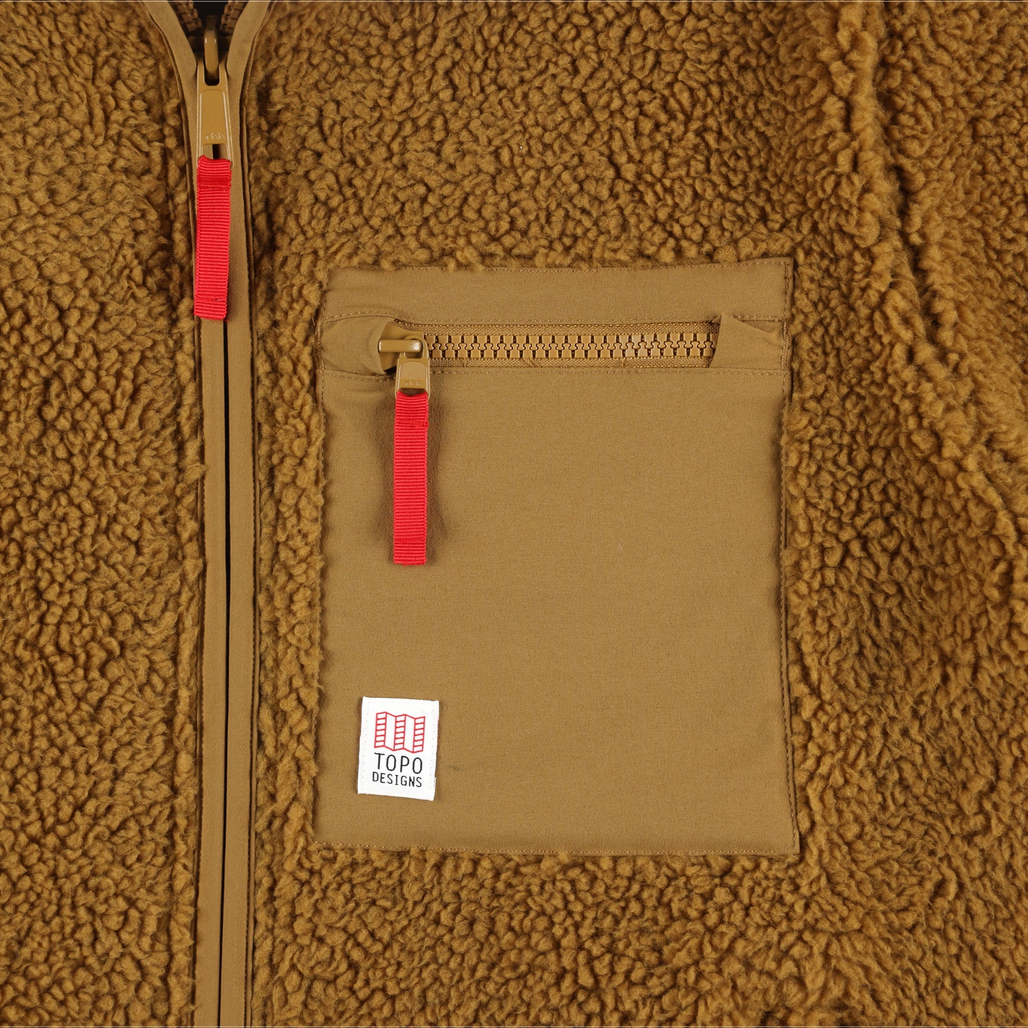 Detail shot of Topo Designs Men's Sherpa Jacket in "dark khaki" brown showing sherpa fleece side, zipper, and chest zipper pocket with logo patch..