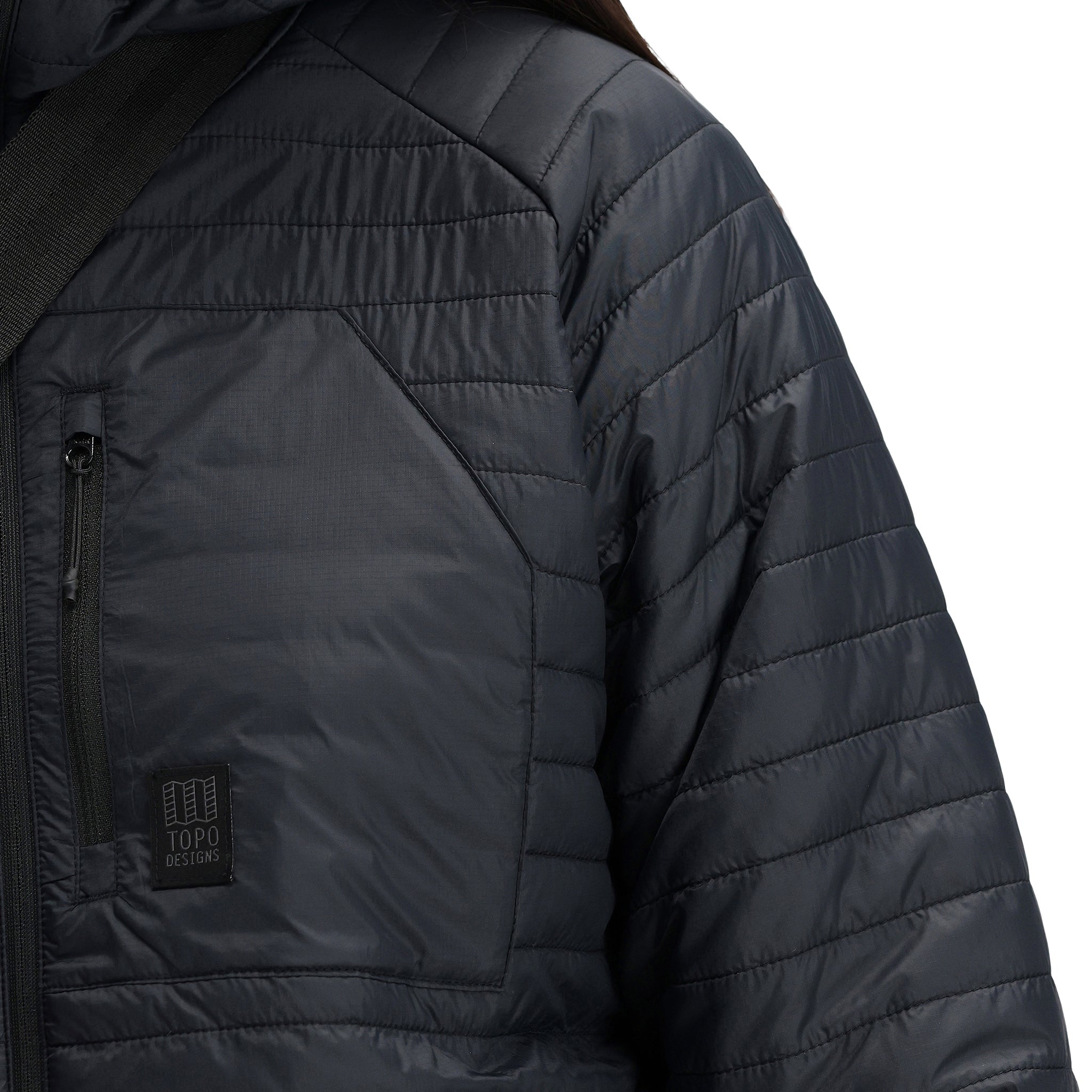 General detail shot of chest zipper pocket and logo patch on Topo Designs Women's Global Puffer recycled insulated packable Hoodie jacket in "black"