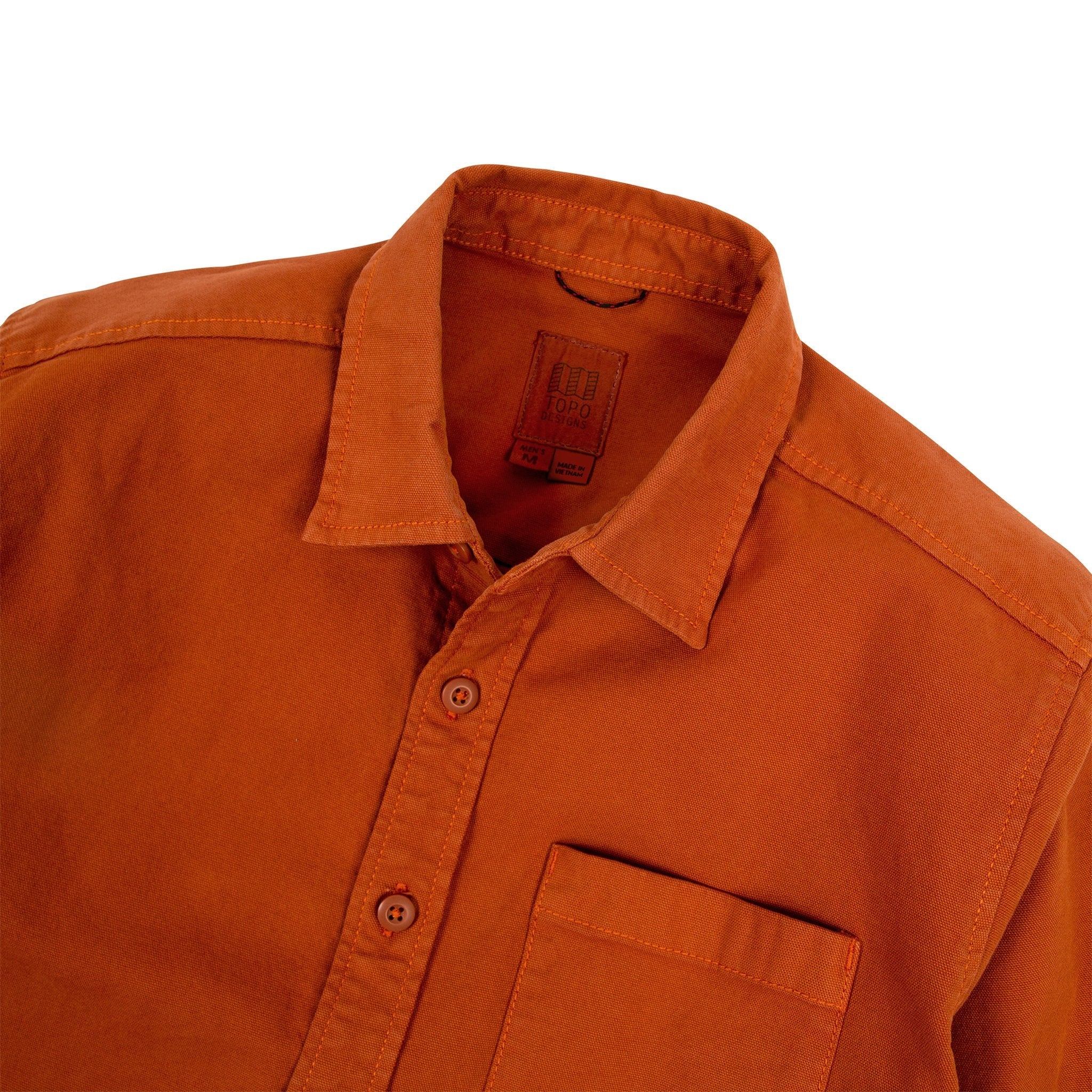 Detailaufnahme des Topo Designs Herren Dirt Shirt in Brick Orange mit Kragen, Innenschild, Knöpfen und Brusttasche.