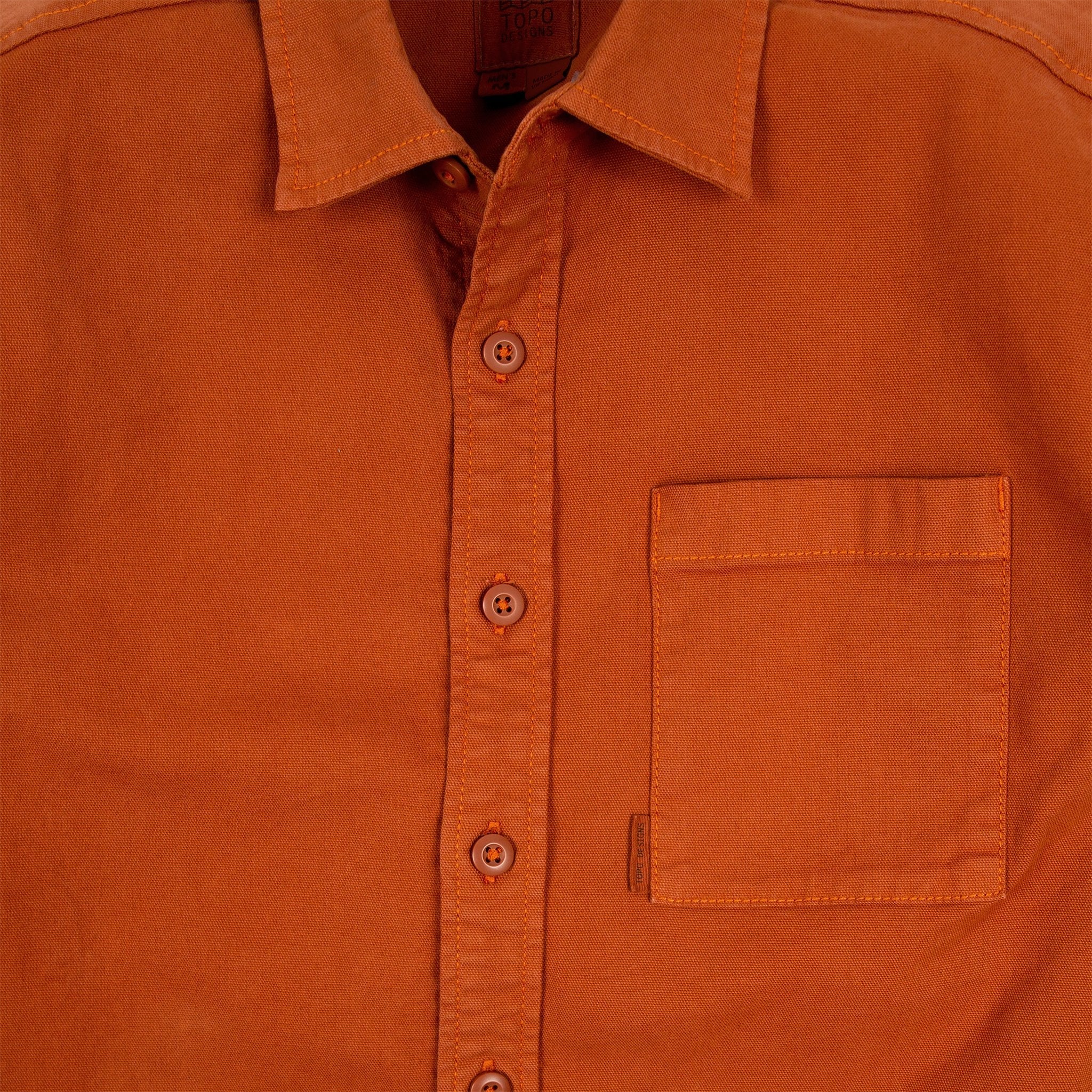 Detailaufnahme des Topo Designs Herren Dirt Shirt in Brick Orange mit Knöpfen und Brusttasche.