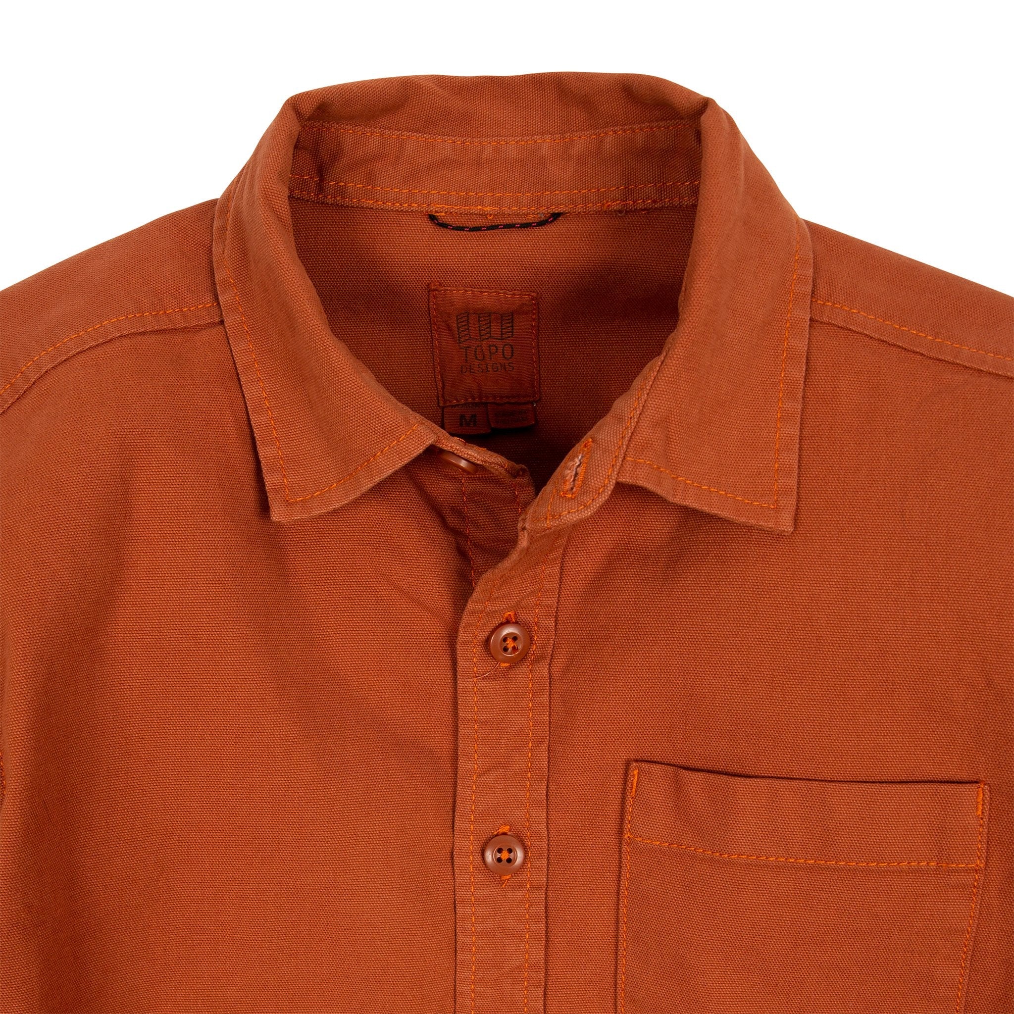 Allgemeine Detailaufnahme des Topo Designs Herren Dirt Shirt in Brick Orange mit Kragen, Knöpfen und Brusttasche.