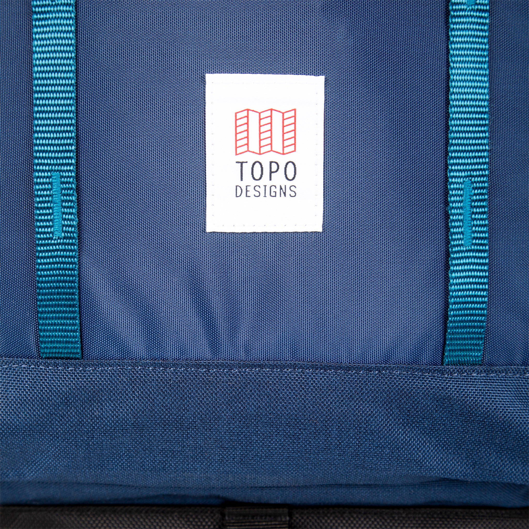 Gesamtansicht des Topo Designs Logoaufnähers und des vorderen Daisy-Chain-Gurtbandes auf dem Global Travel Bag 40L Durable Carry On Convertible Laptop Travel Backpack in Marineblau.