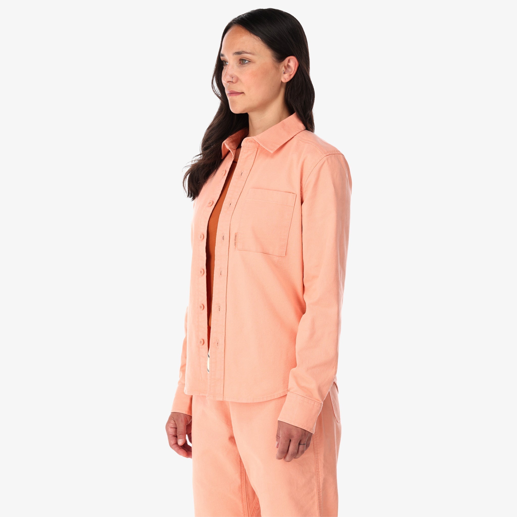 Topo Designs Damen Dirt Shirt langärmeliges Button-up aus Stretch-Baumwolle in "peach" pink auf der Modellseite.