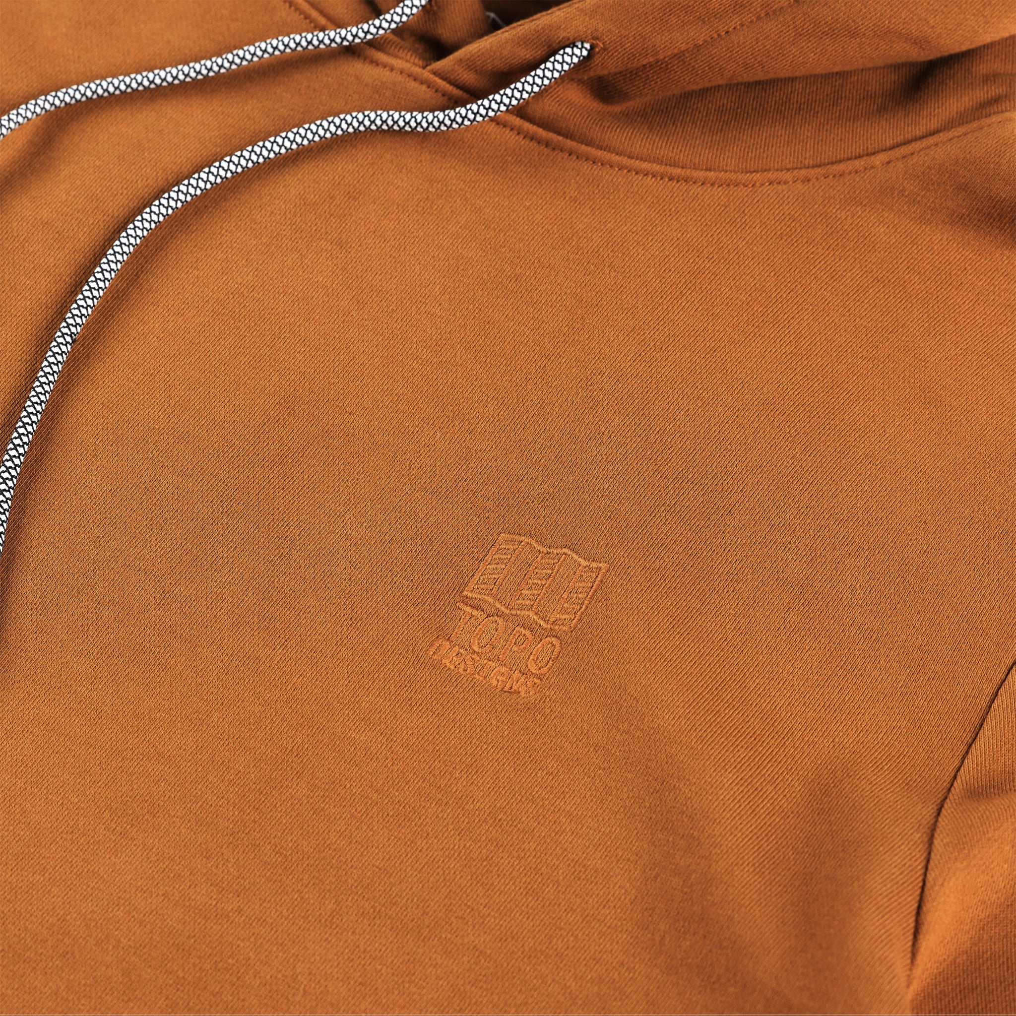 Detailaufnahme des gestickten Brustlogos auf dem Topo Designs Herren Dirt Hoodie 100% Bio-Baumwolle French Terry Sweatshirt in "Earth" braun. Auf "Pond Blue" anzeigen.