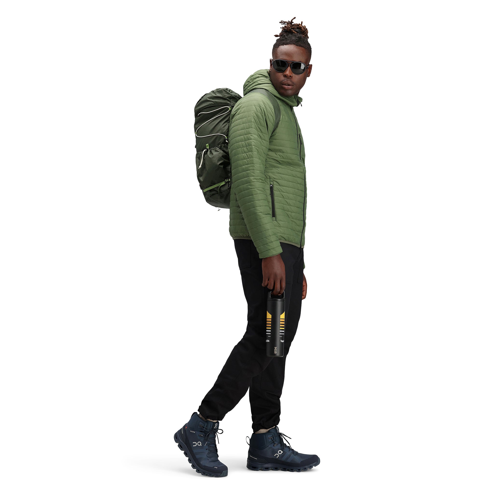 Model trägt Topo Designs Herren Global Puffer packbare recycelte isolierte Hoodie Jacke in "olive" grün.