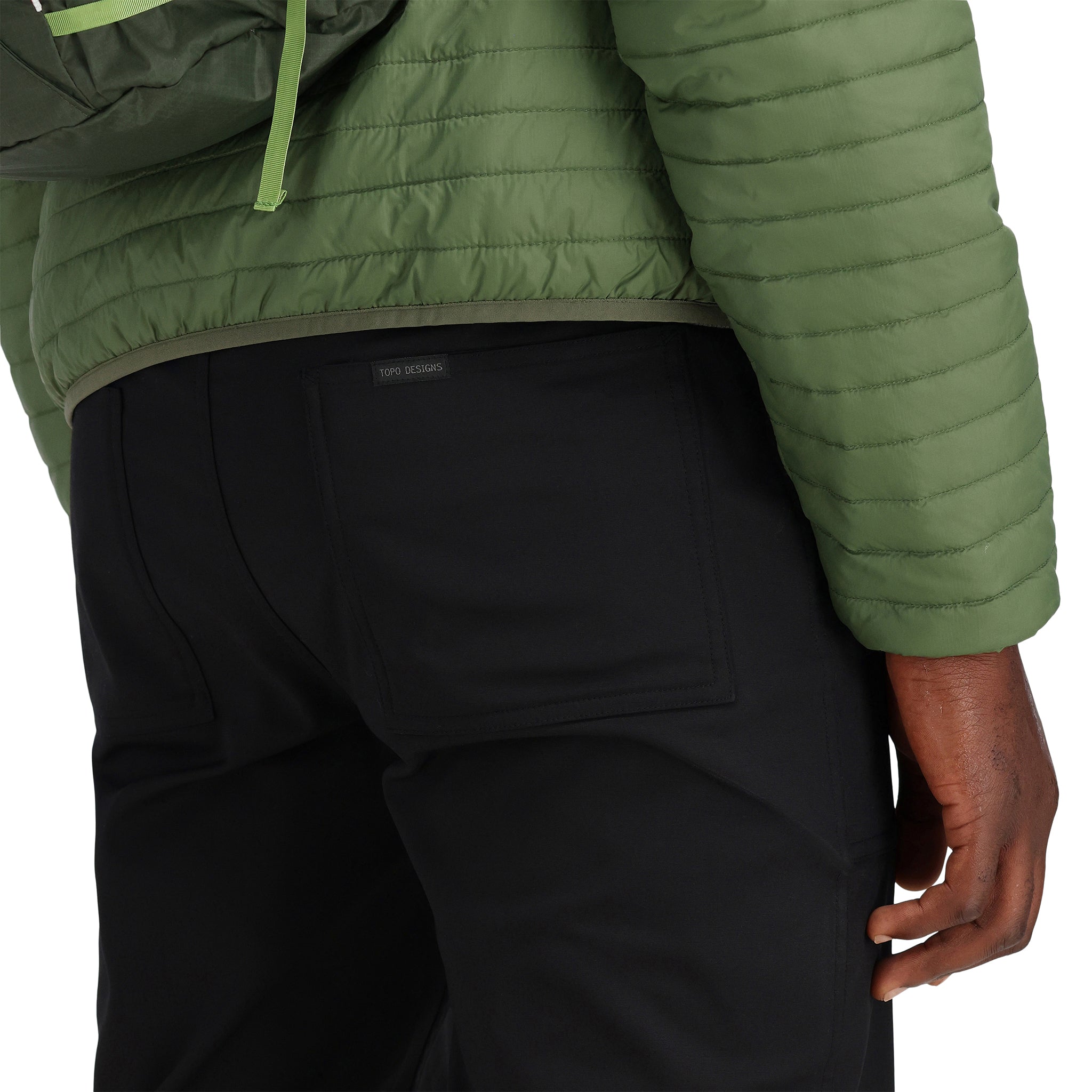 Allgemeine Detailaufnahme des unteren Saums am Model, das die Topo Designs Herren Global Puffer packbare recycelte isolierte Hoodie Jacke in "olive" grün trägt.