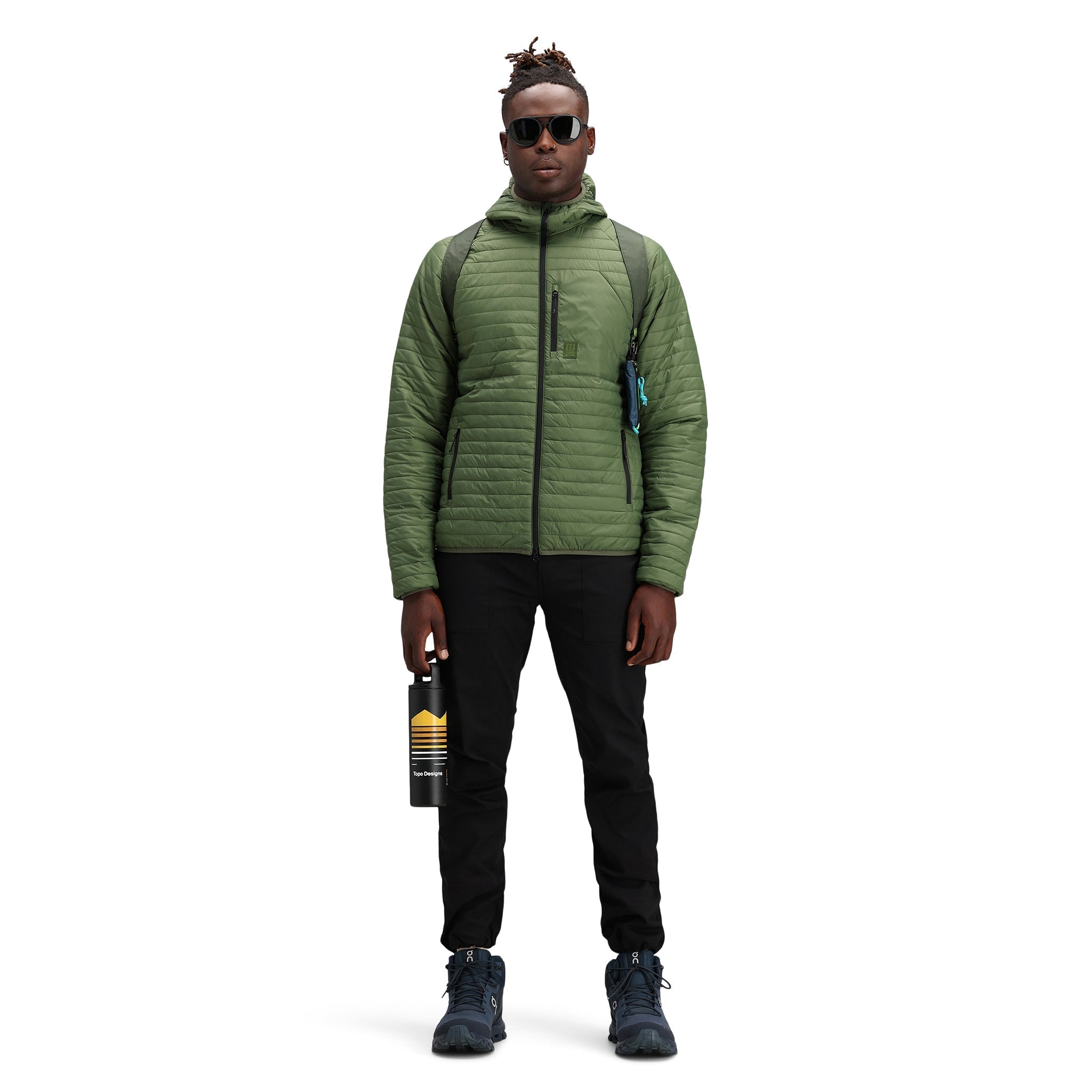 Model trägt Topo Designs Herren Global Puffer packbare recycelte isolierte Hoodie Jacke in "olive" grün.