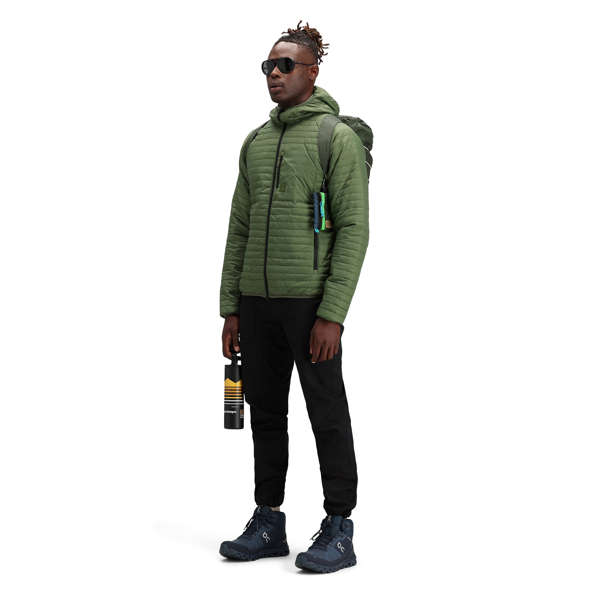 Model trägt Topo Designs Herren Global Puffer packbare recycelte isolierte Hoodie Jacke in "olive" grün.