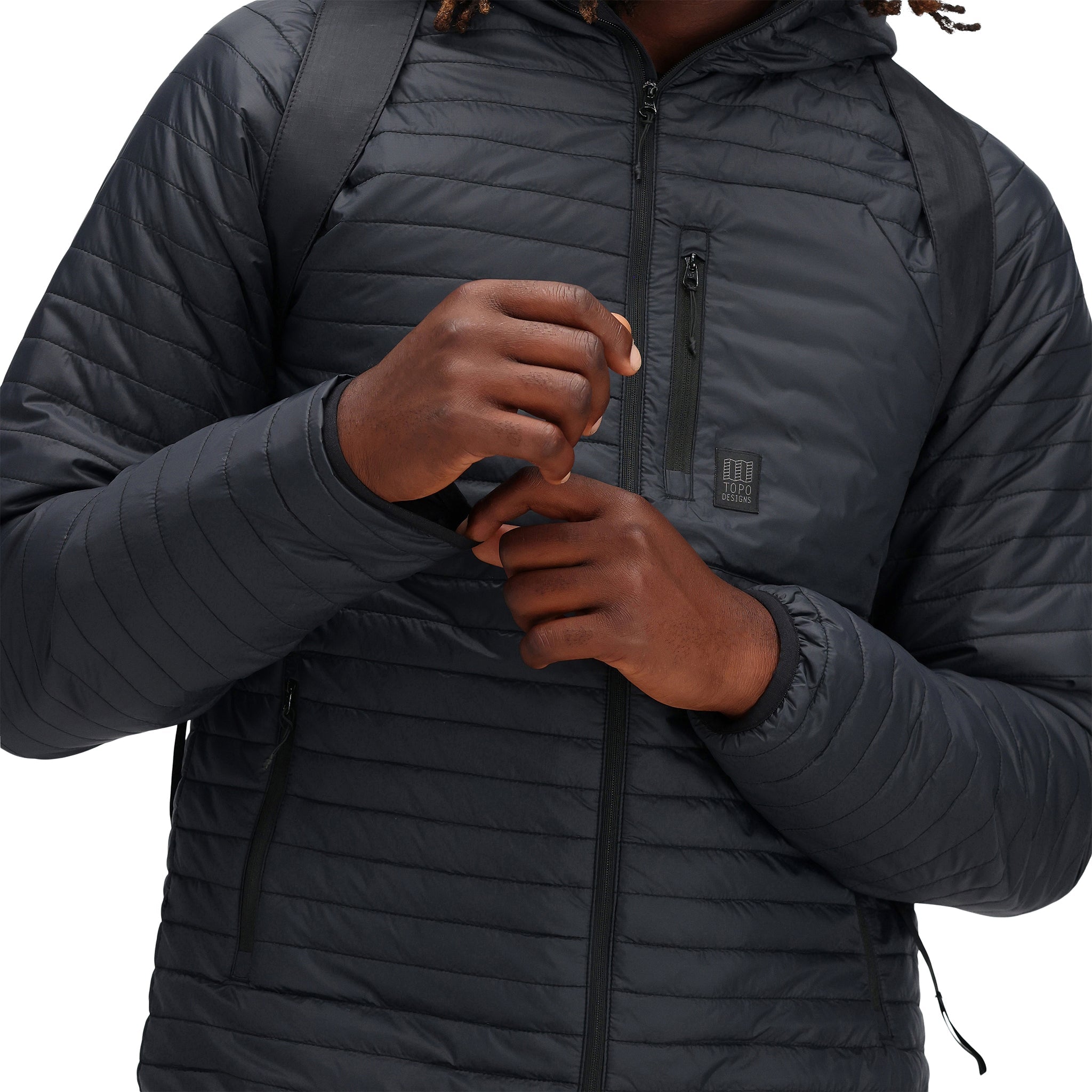 Allgemeine Aufnahme des Bündchendetails am Model, das die Topo Designs Herren Global Puffer packbare recycelte isolierte Hoodie Jacke in "schwarz" trägt