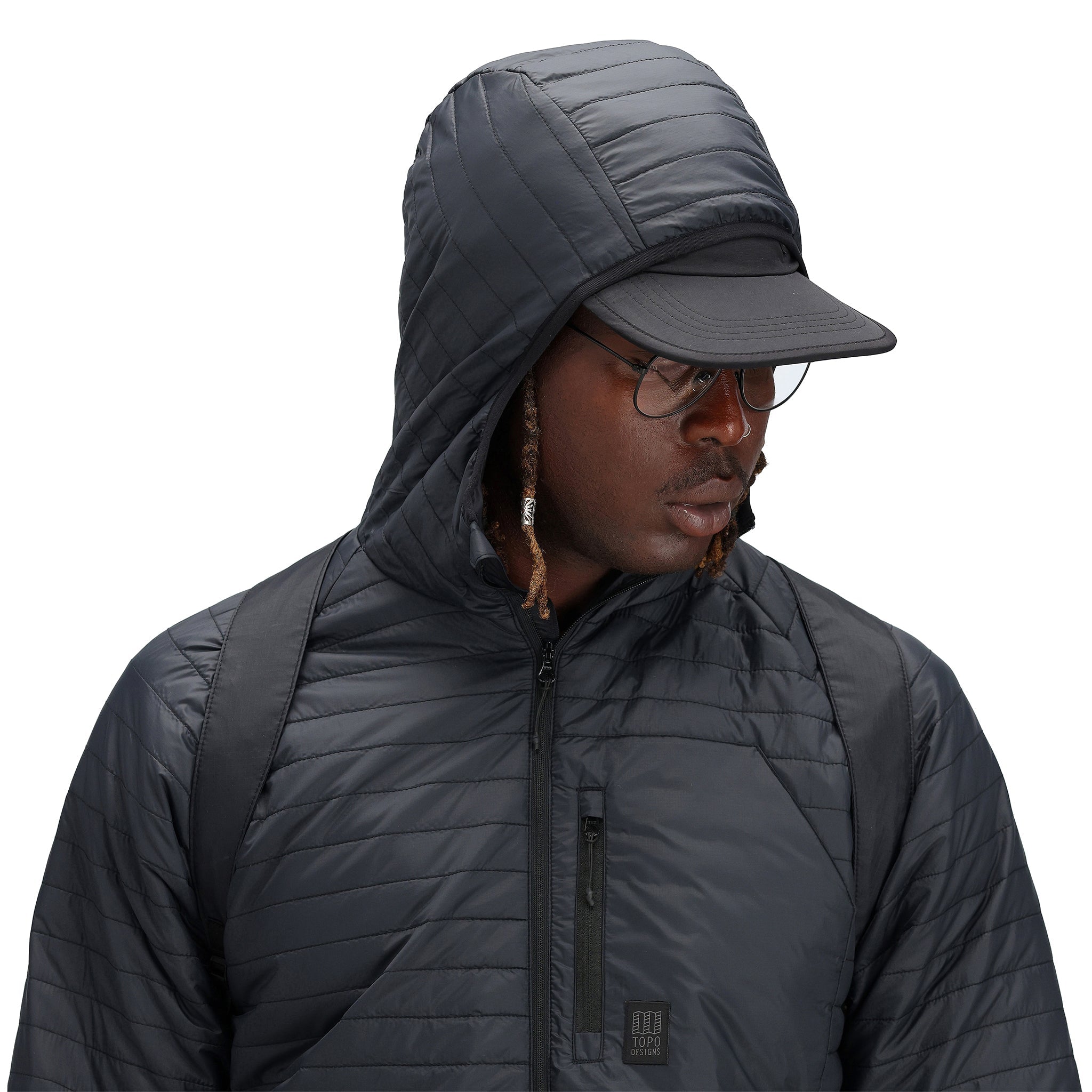 Detailaufnahme der Kapuze des Models, das die Topo Designs Herren Global Puffer packbare recycelte isolierte Hoodie Jacke in "schwarz" trägt