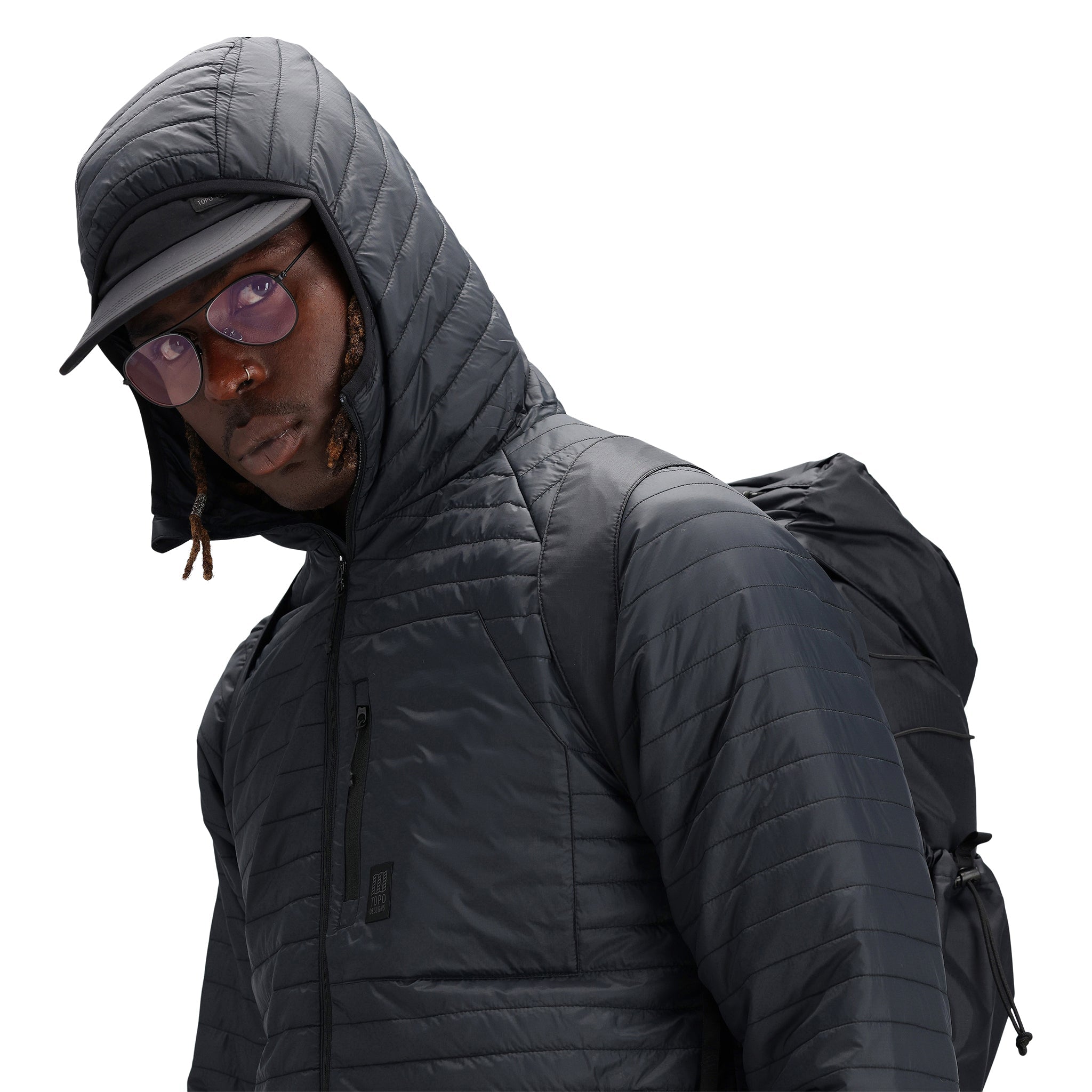 Detailaufnahme der Kapuze des Models, das die Topo Designs Herren Global Puffer packbare recycelte isolierte Hoodie Jacke in "schwarz" trägt