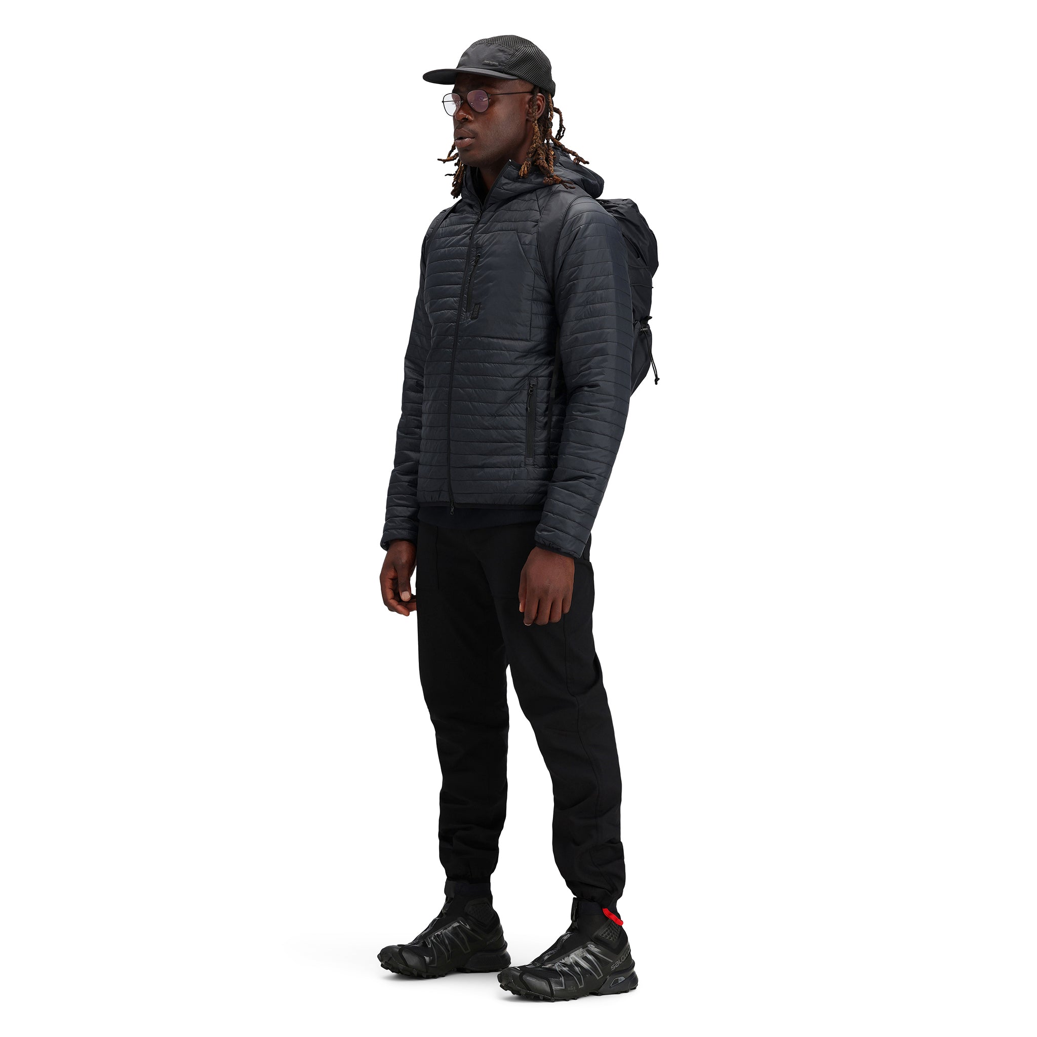 Model trägt Topo Designs Herren Global Puffer packbare recycelte isolierte Hoodie Jacke in "schwarz".