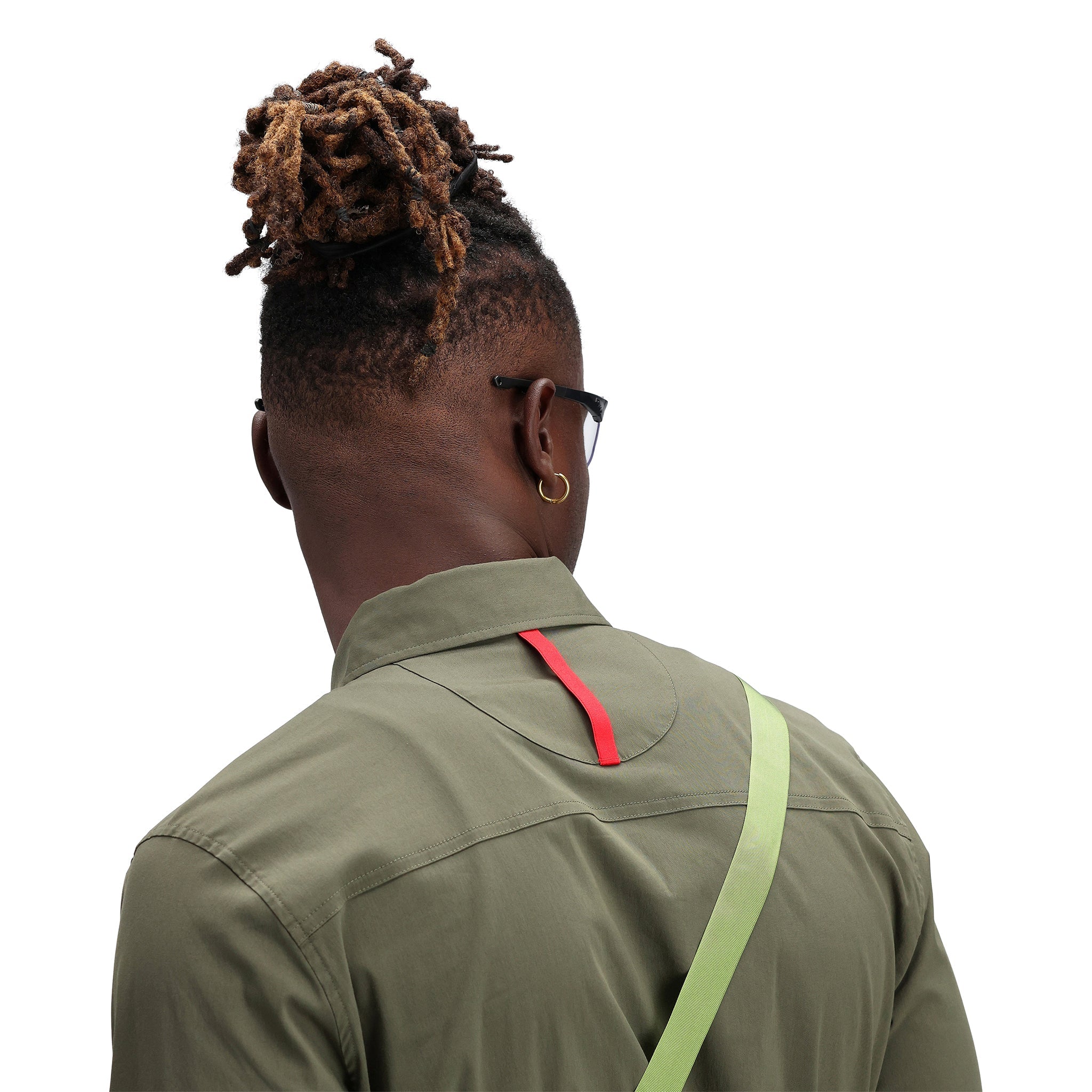 Detailaufnahme des Packfast-Packbandes auf dem Rücken des Modells, das das Topo Designs Herren Global Shirt Langarm-Leichtgewicht-Reise-Snap-Shirt in "olive" grün trägt.