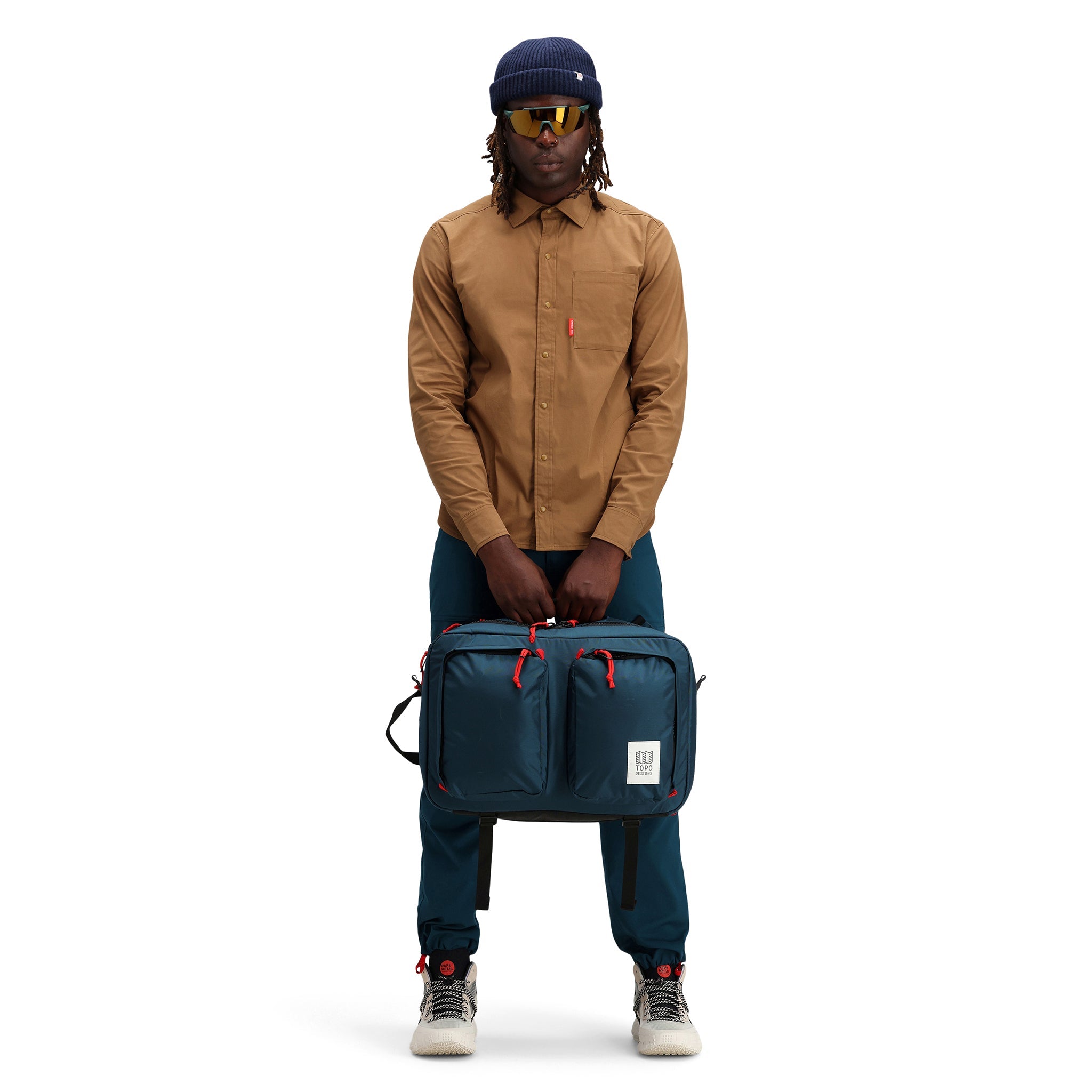 Allgemeine Modellaufnahme der Vorderseite, die das Tragen des Topo Designs Global Briefcase Convertible Laptop-Reiserucksacks in "Navy" blauem Nylon zeigt.