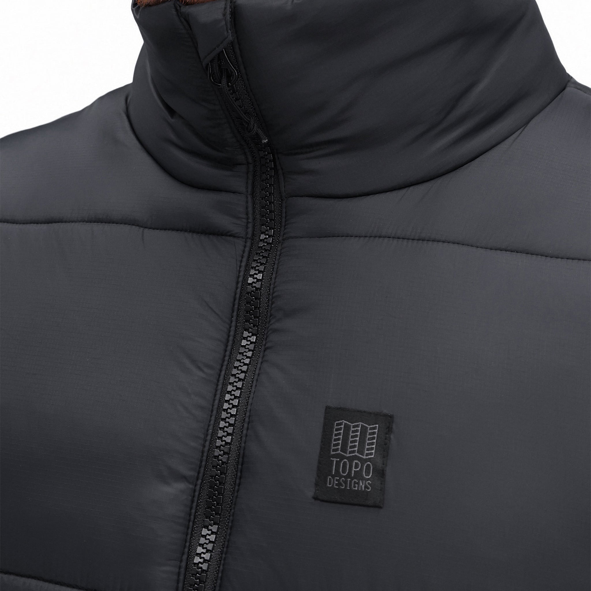 Detailaufnahme der Vorderseite der Topo Designs Herren Mountain Puffer recycled insulated Vest in "Black" mit Reißverschluss und Brustlogo.