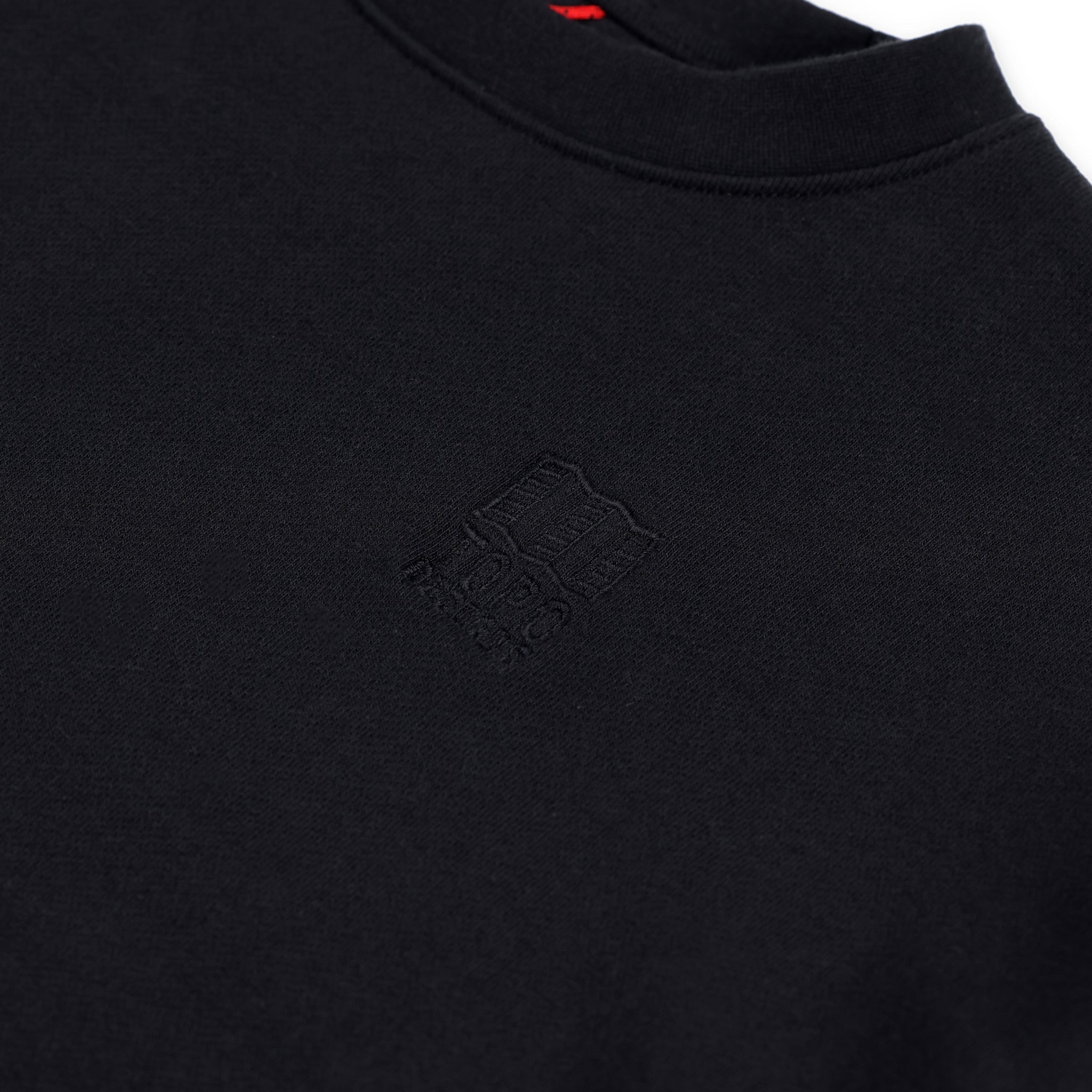 Detailaufnahme des gestickten Brustlogos auf dem Topo Designs Damen Dirt Crew Sweatshirt aus 100% Bio-Baumwolle French Terry in "schwarz".