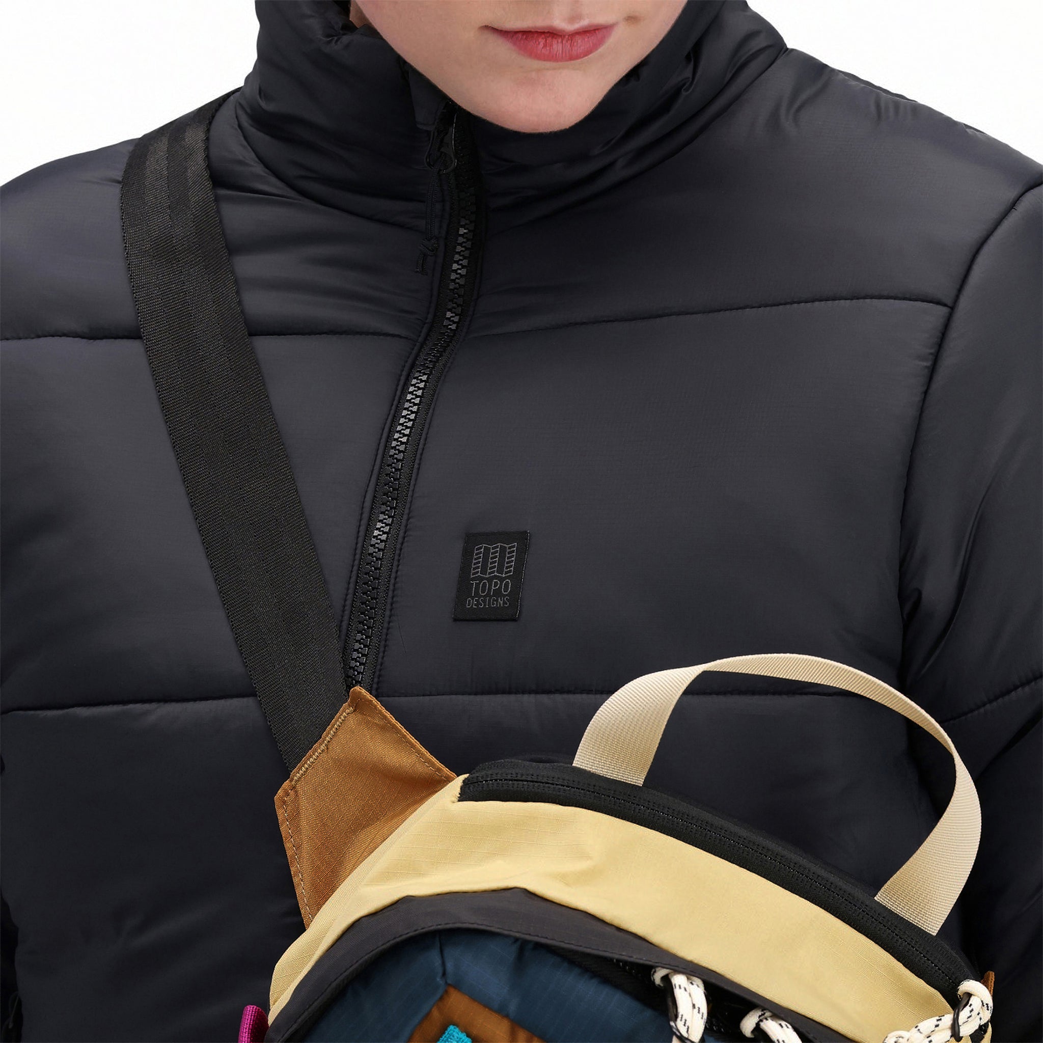 Vordere Modellaufnahme der Topo Designs Damen Puffer recycled insulated Jacket in "Black" mit Reißverschluss und Brustlogo.