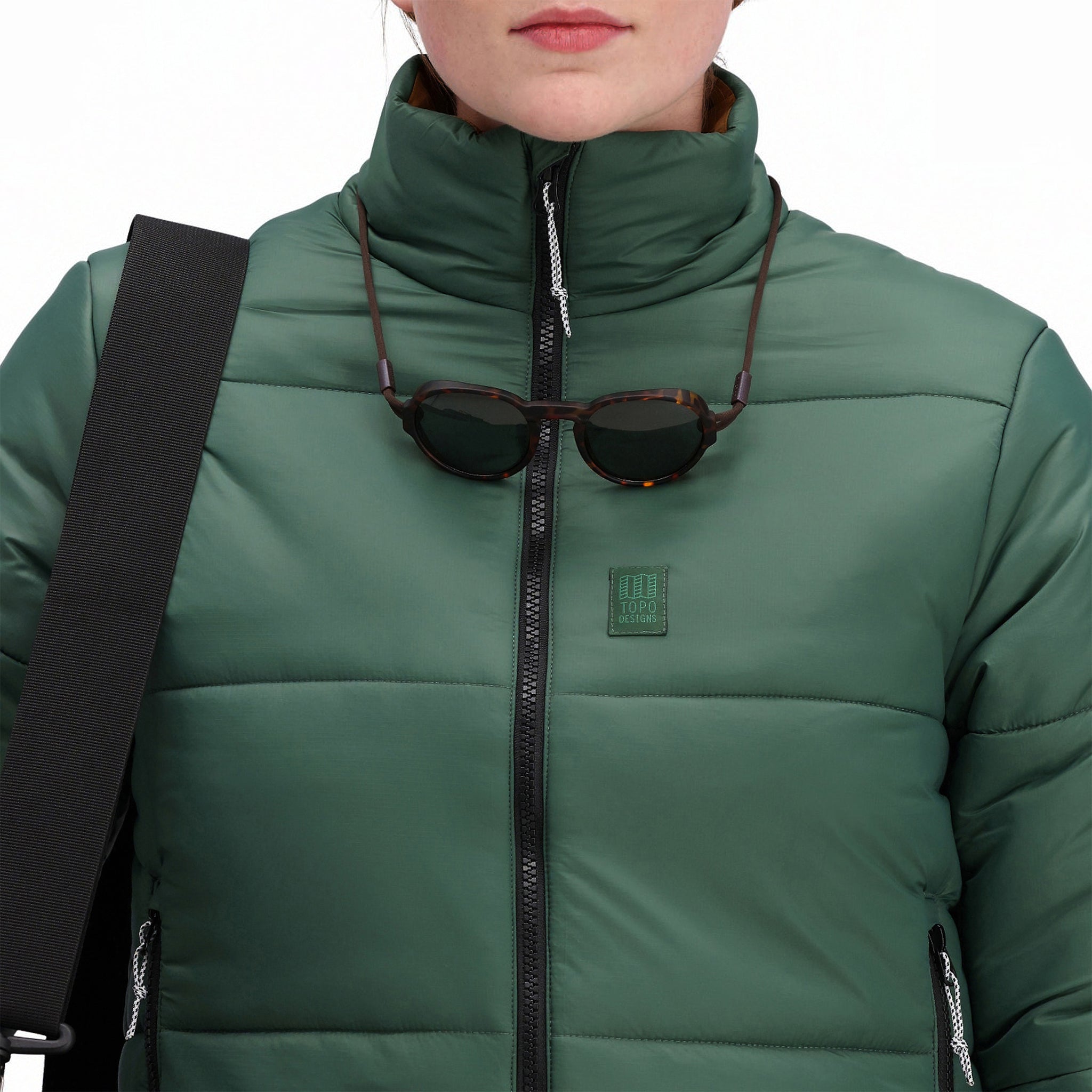 Vordere Modellaufnahme der Topo Designs Damen Puffer-Recycling-Isolationsjacke in "Forest" grün mit Reißverschluss, Kragen und Brustlogo.