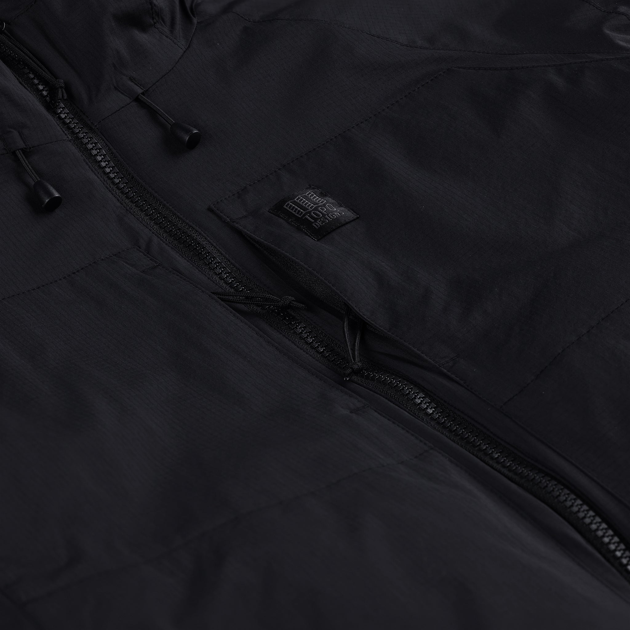 Detailaufnahme der Brust-Reißverschlusstasche der Topo Designs Damen Puffer Primaloft insulated Hoodie Jacke in "black"