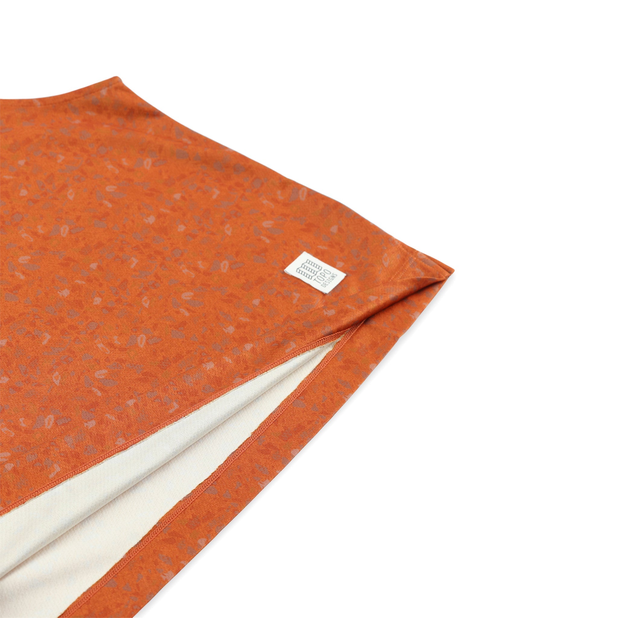 Gesamtansicht des Topo Designs Logoaufnähers auf dem Damen 30+ UPF feuchtigkeitsableitenden River Tank Top in clay orange terrazzo print.