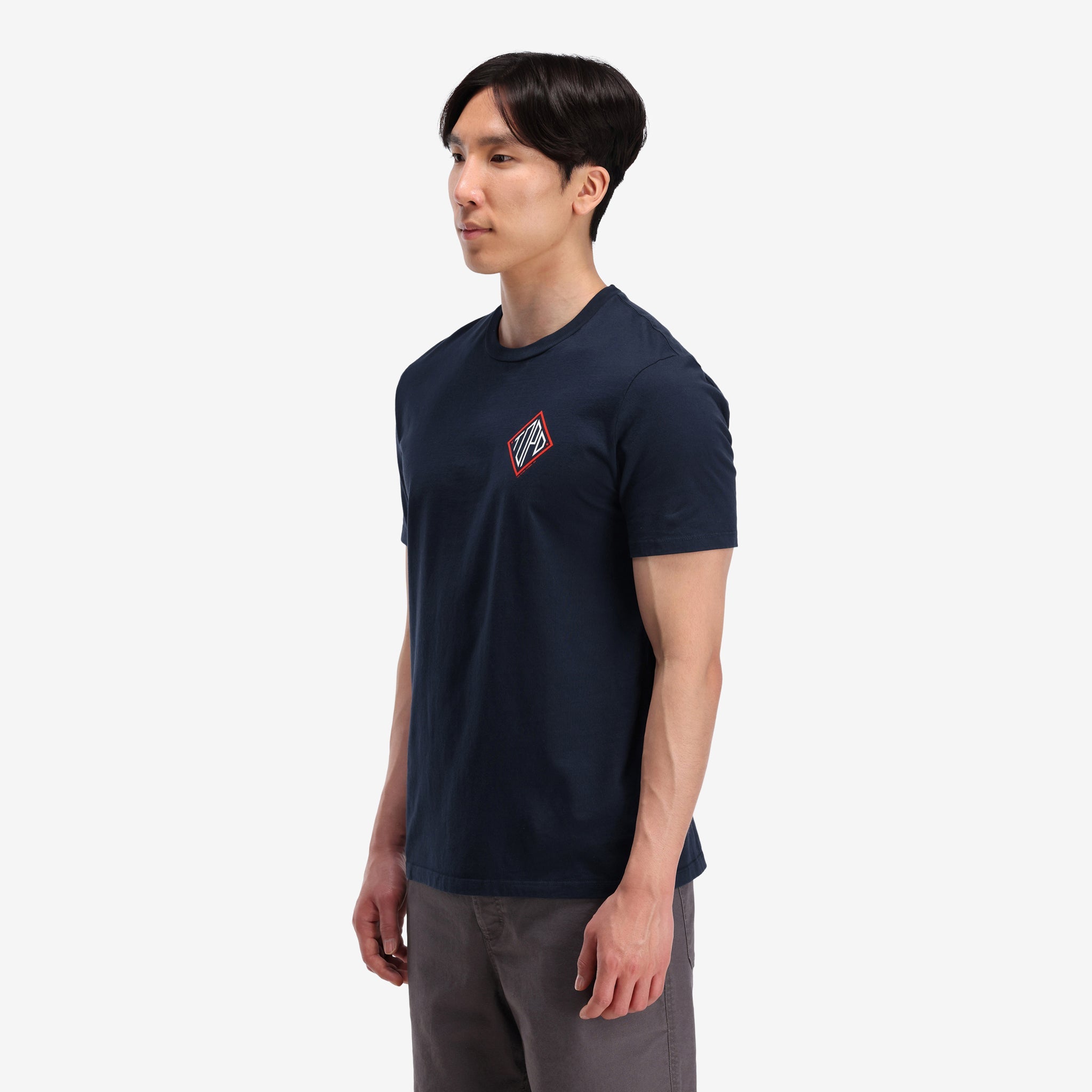 Allgemeine Aufnahme, auf Modell linke Seitenansicht von Topo Designs Herren Small Diamond Tee 100% Bio-Baumwolle Kurzarm-Grafik-Logo-T-Shirt in "navy" blau.